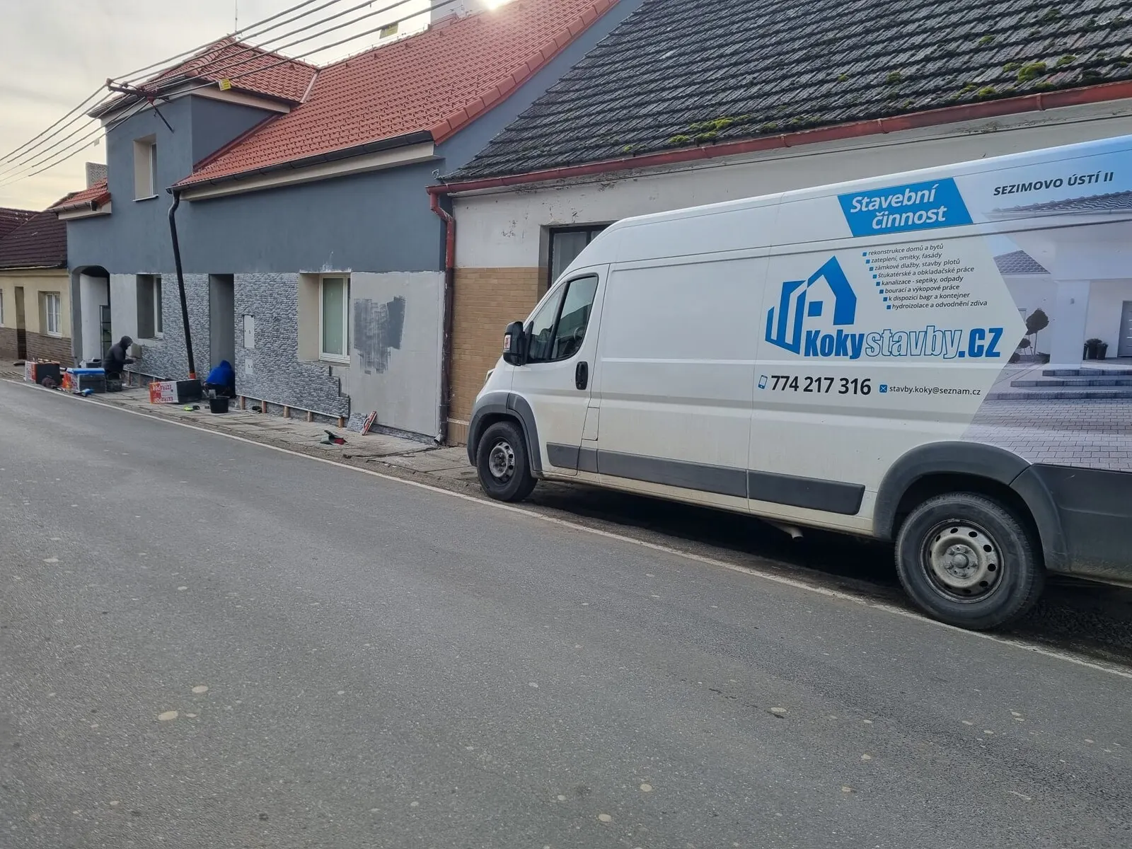 Rozpracovaná fasáda řadového domu s vyspravenými plochami a dodávkou před domem