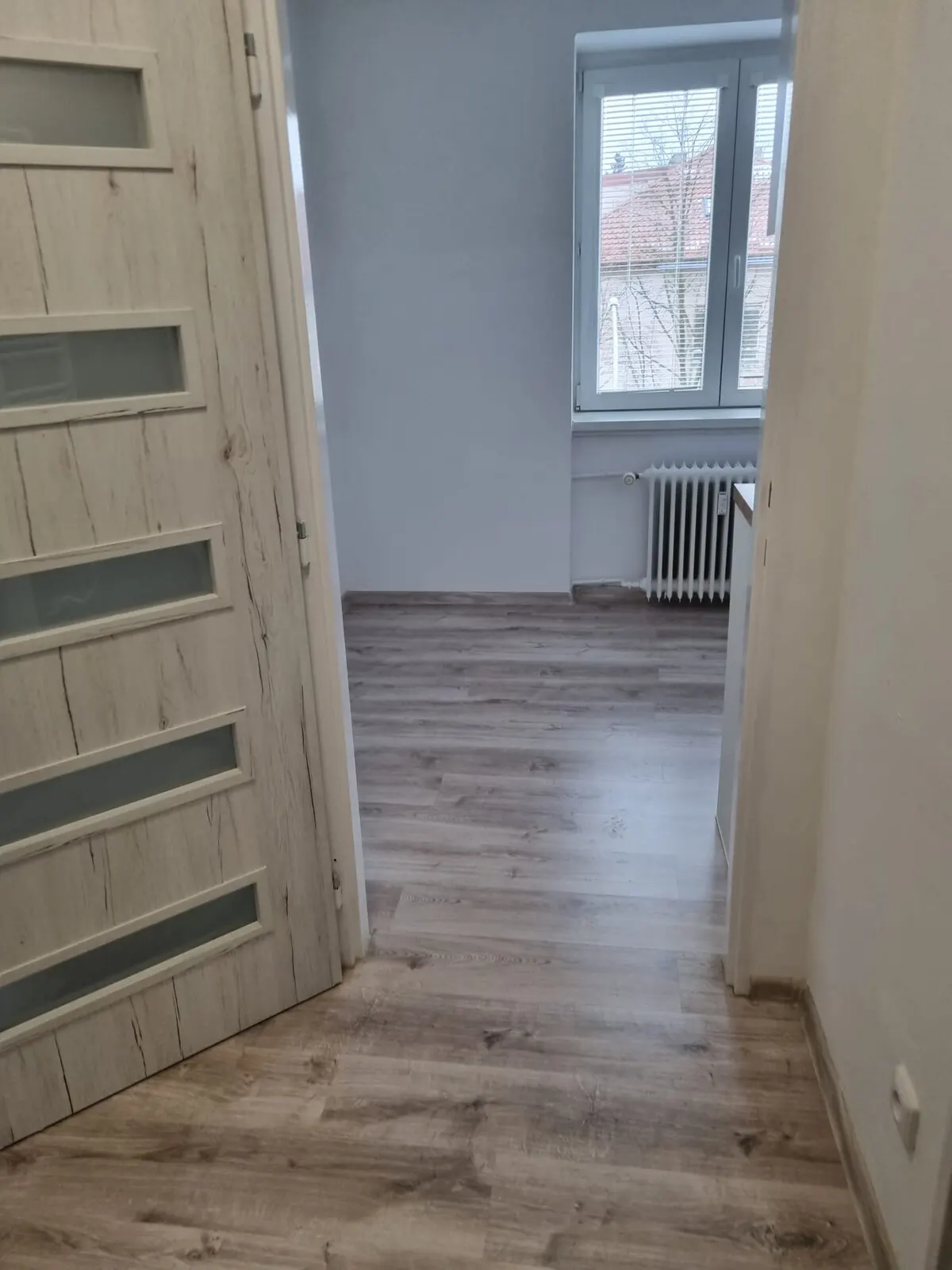 Vyklizený pokoj po rekonstrukci s vinylovou podlahou, novým oknem a radiátorem