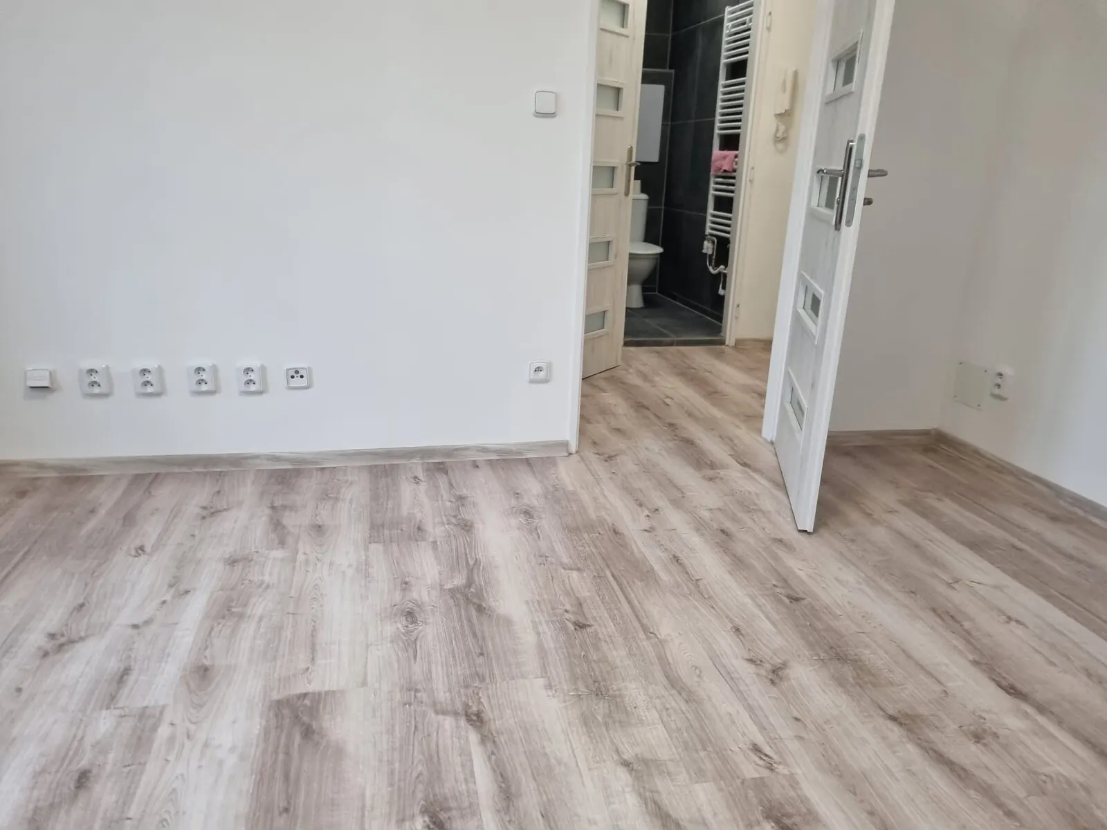 Pokoj s vinylovou podlahou a otevřenými dveřmi do nové koupelny