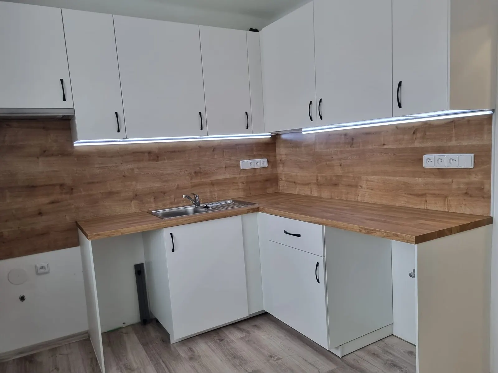 Nová bílá kuchyňská linka s dřevěnou pracovní deskou a osvětlením pod skříňkami