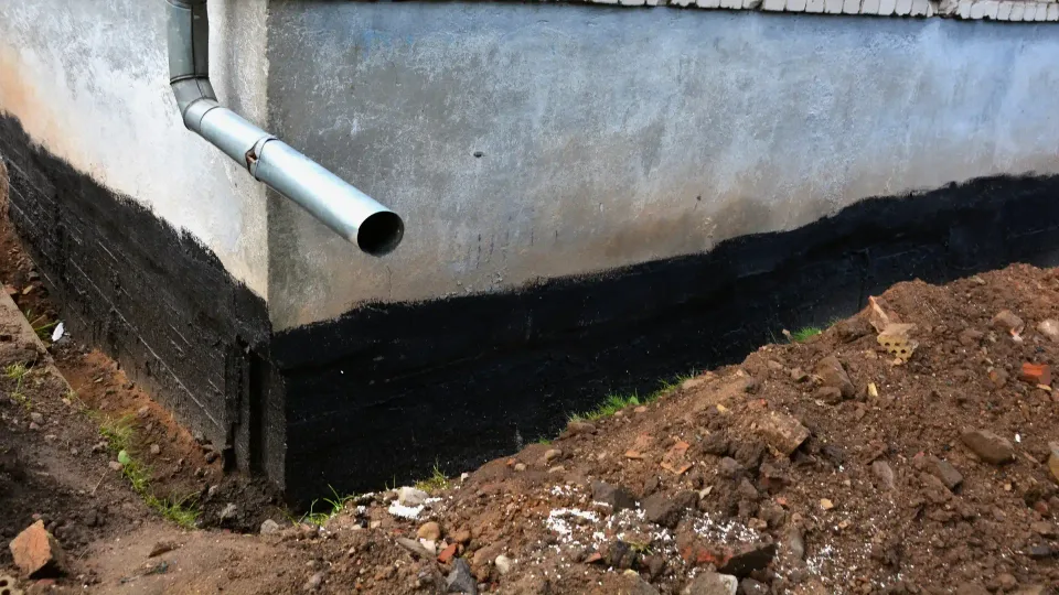 Základové zdivo s natřenou černou hydroizolací a drenážní trubkou v otevřeném výkopu